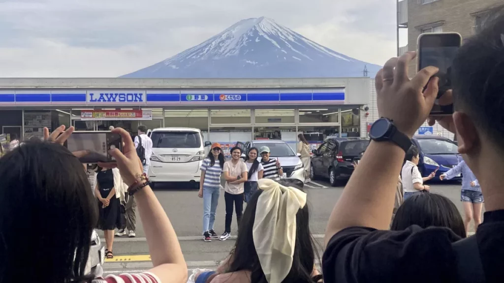 Visitors take a photo in front of a convenient store at Fujikawaguchiko town, Japan, with a backdrop of Mount Fuji.