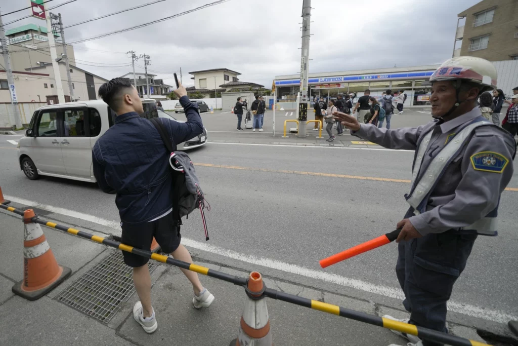 Photo 1 : A security guard redirects a tourist outside of the construction site of a barricade near the Lawson convenience store. Tuesday, April 30, 2024, at Fujikawaguchiko town, Yamanashi Prefecture, central Japan. 