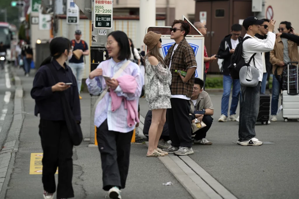 Photo 3 : Tourists hang out outside the Lawson convenience store, a popular photo spot framing a picturesque view of Mt. Fuji in the background on cloudy evening.